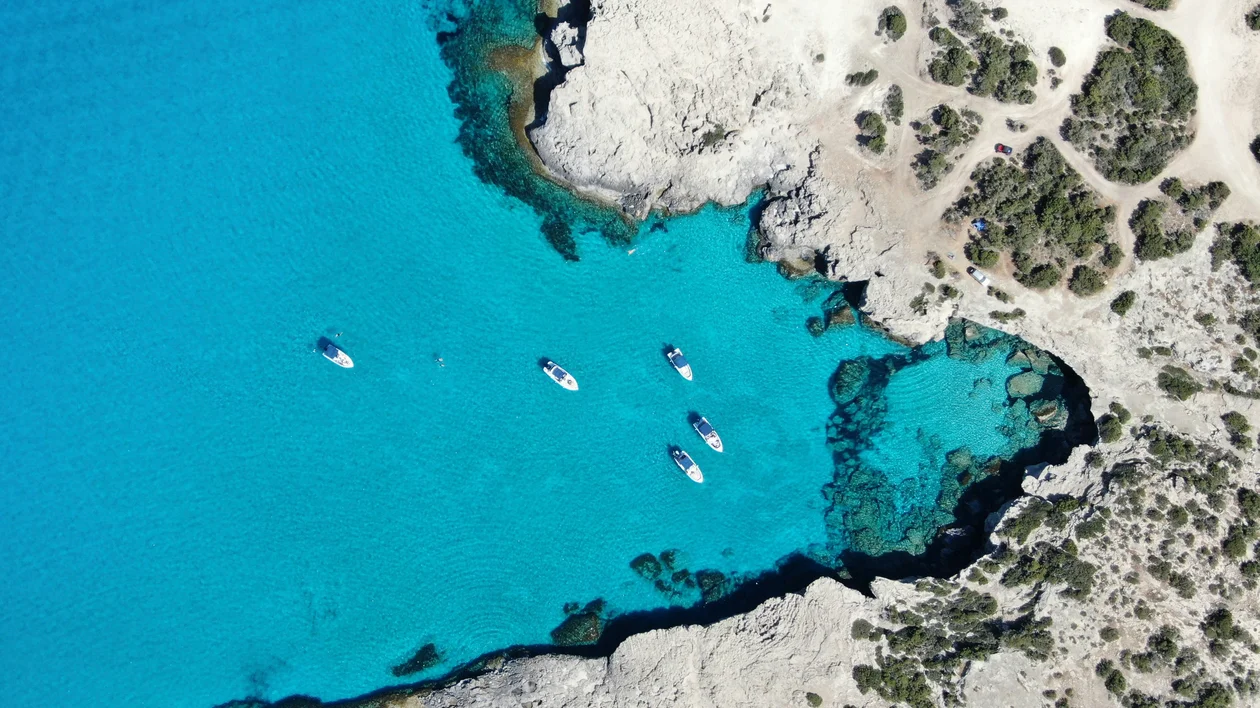 Aerial view of turquoise bay with boats and rocky, sandy shoreline.
