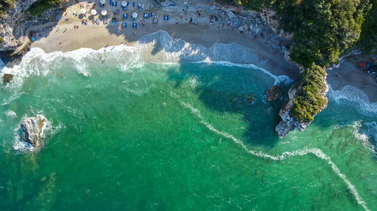 Aerial view of a sandy beach with green waves and sunbathers under umbrellas.