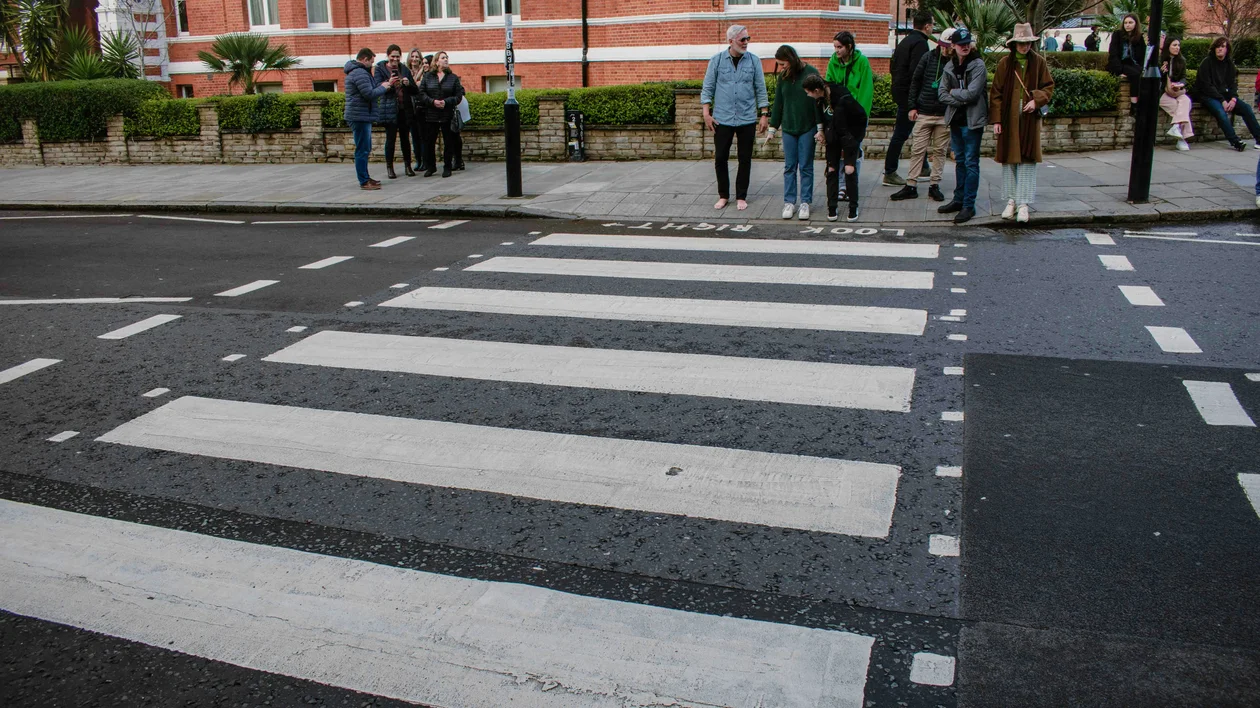 People standing at a zebra crossing on a city street with a red brick building in the background.