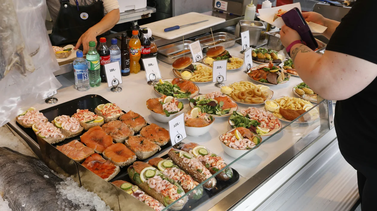 Deli counter with assorted open sandwiches and salads, people choosing food.