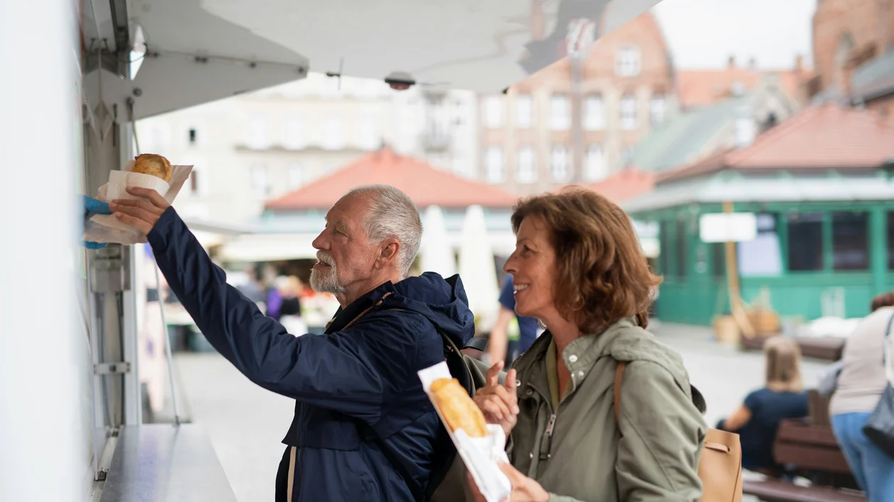 Older couple buys pastries at an outdoor food truck in a city square.