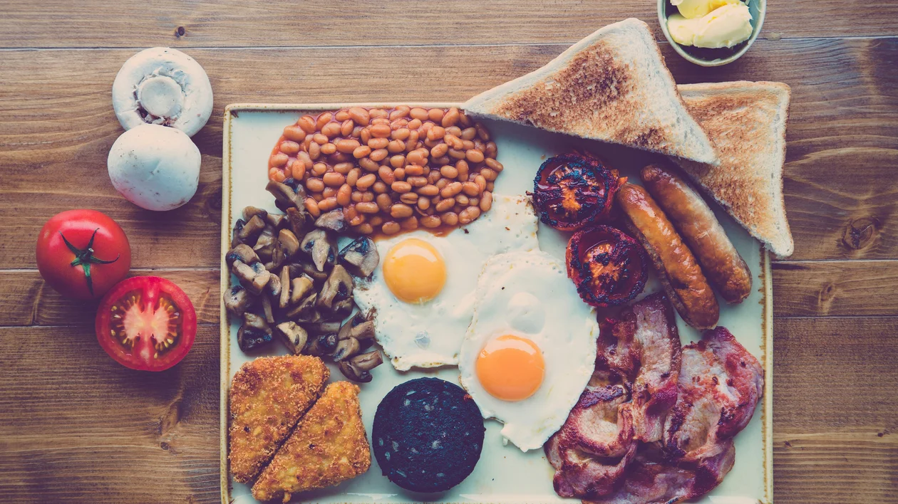 English breakfast with eggs, bacon, sausage, toast, beans, mushrooms, and tomatoes.
