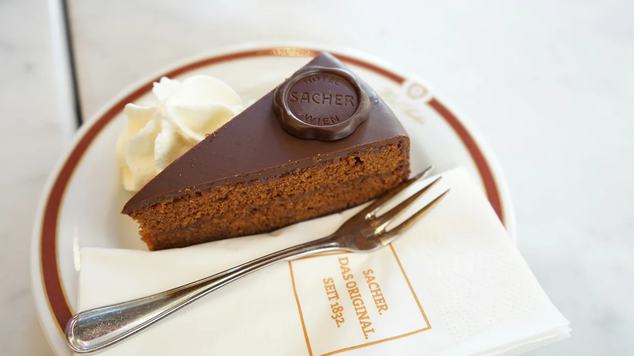 Slice of chocolate cake with whipped cream on a plate, fork and napkin beside it.