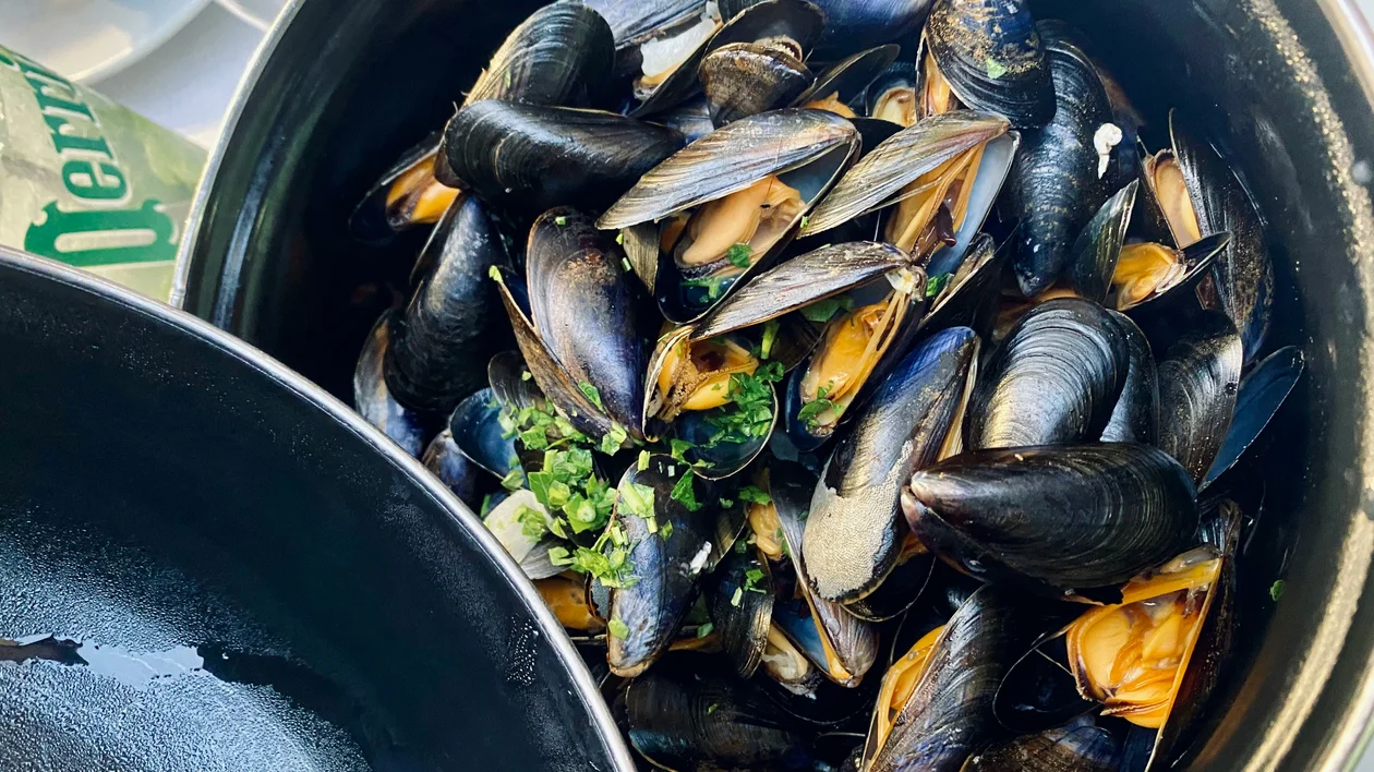 Steamed mussels in a black pot, garnished with chopped herbs.