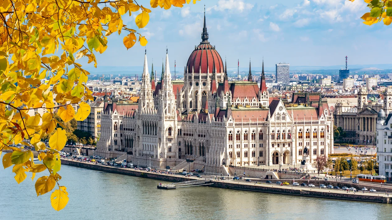 Hungarian Parliament building by the river with autumn leaves in the foreground.