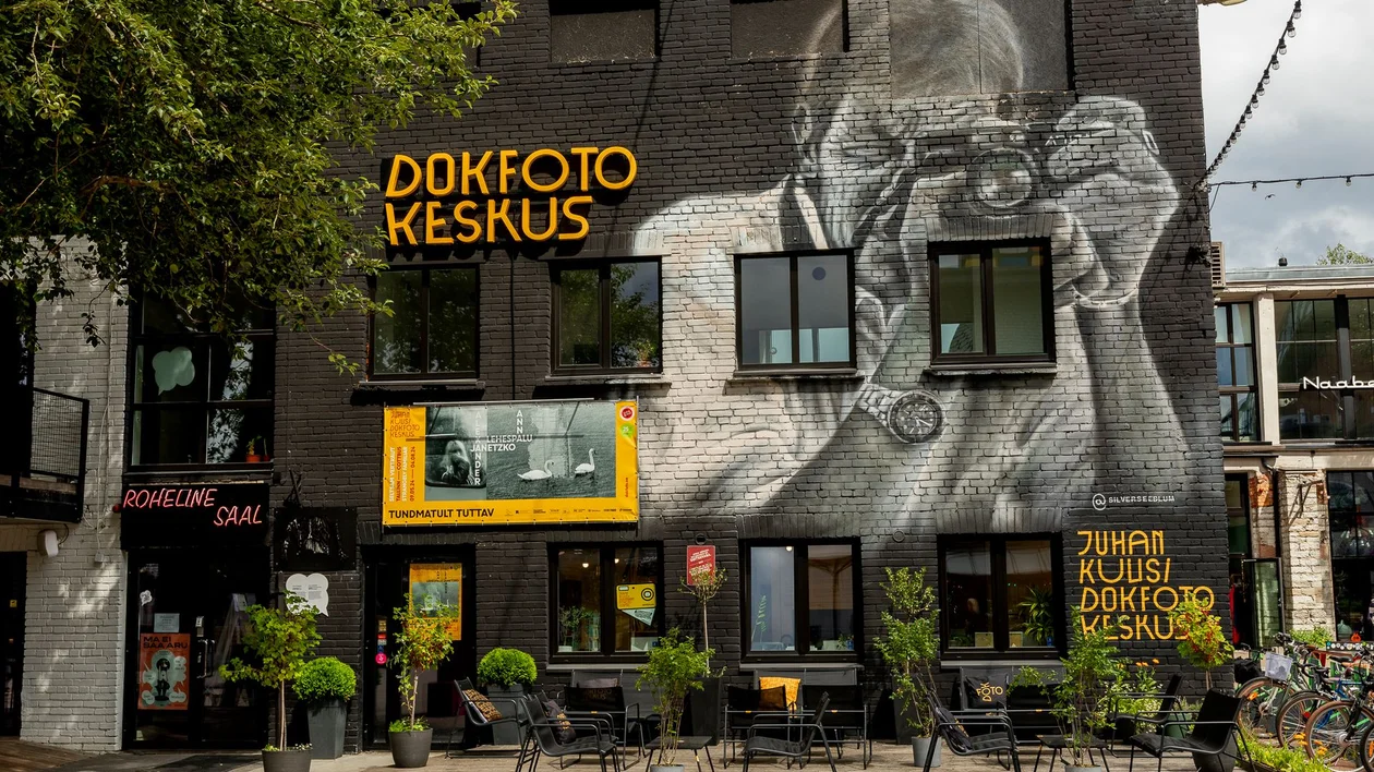 Large mural of a photographer on a black building with outdoor tables and green plants.