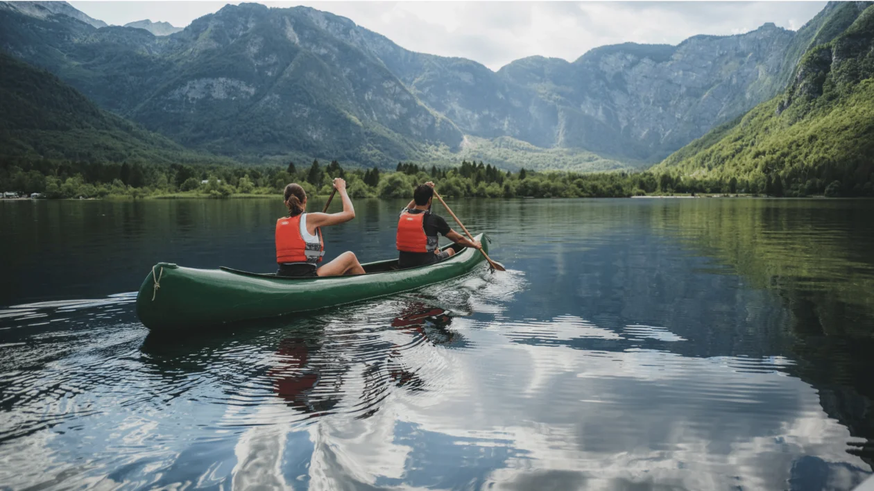 Two people canoeing on a calm lake surrounded by mountains and trees.