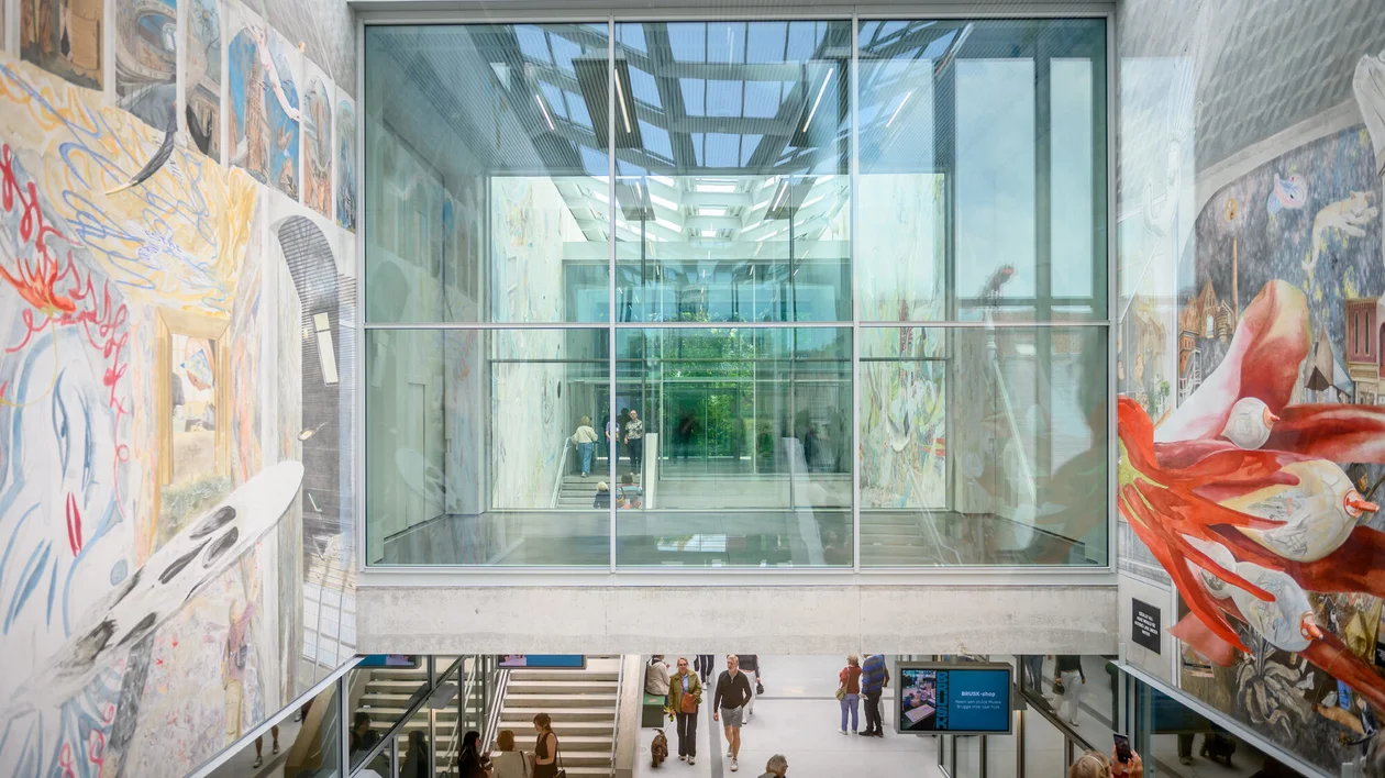 Spacious atrium with glass ceiling, large murals, and people walking below.