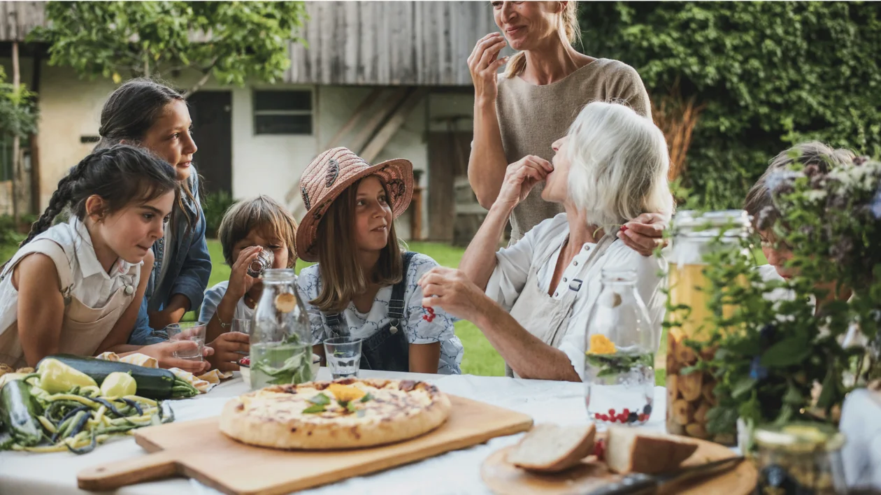 Family enjoying a meal together outdoors, smiling and talking around a table.