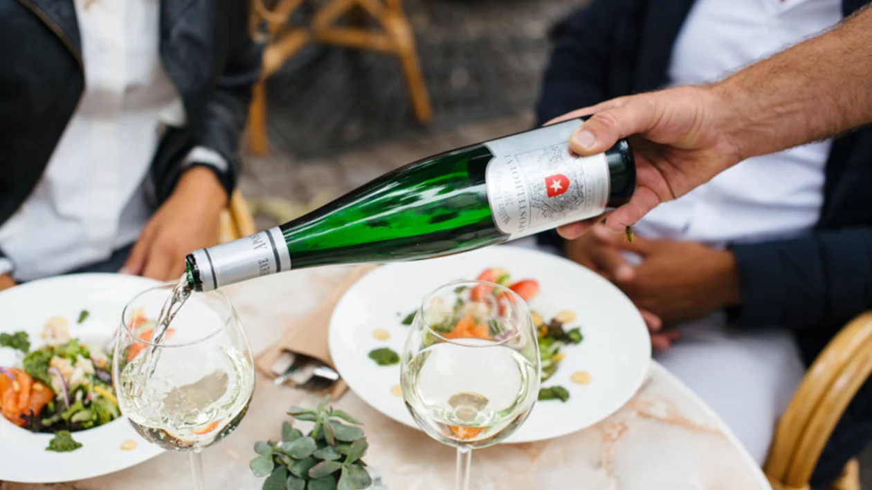 White wine being poured into a glass at an outdoor dining table with plated food.
