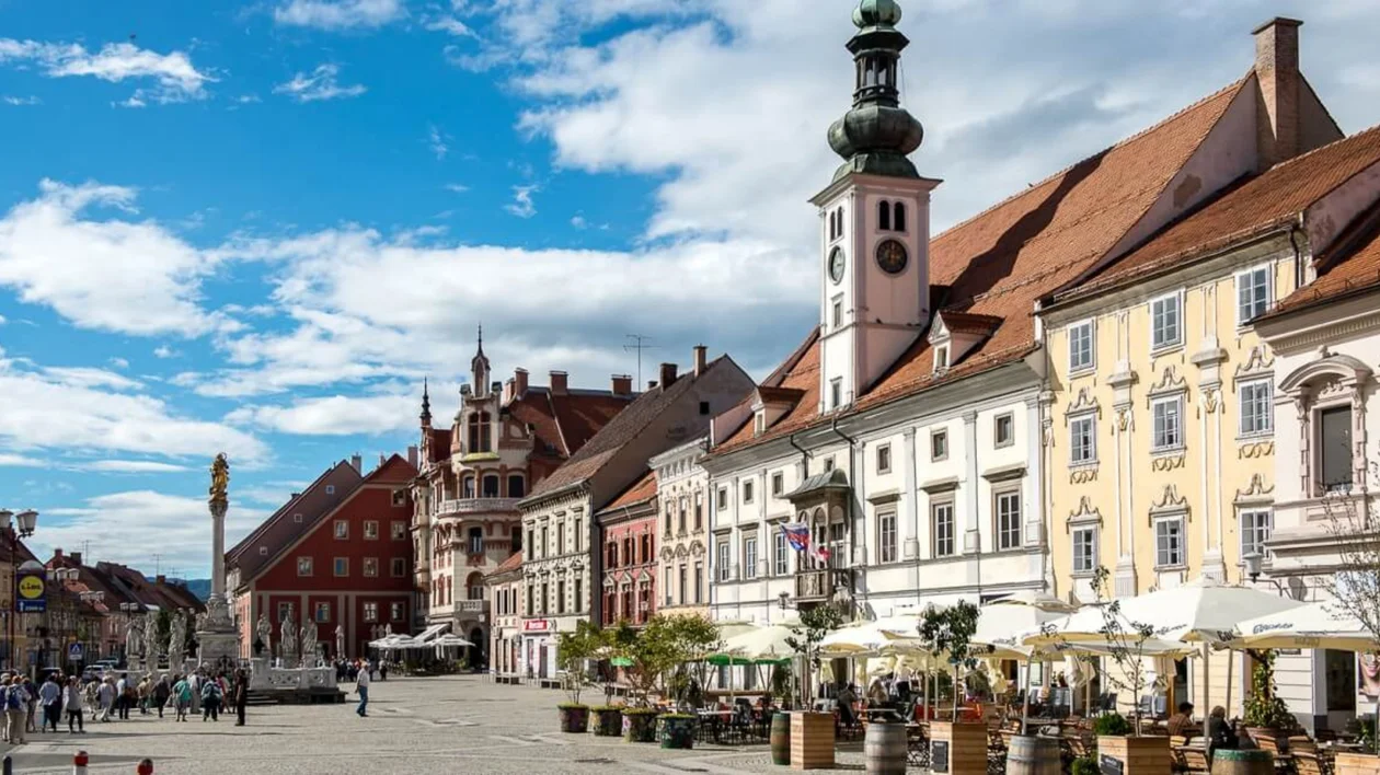 Colorful historic buildings line a sunny European town square with outdoor cafes.