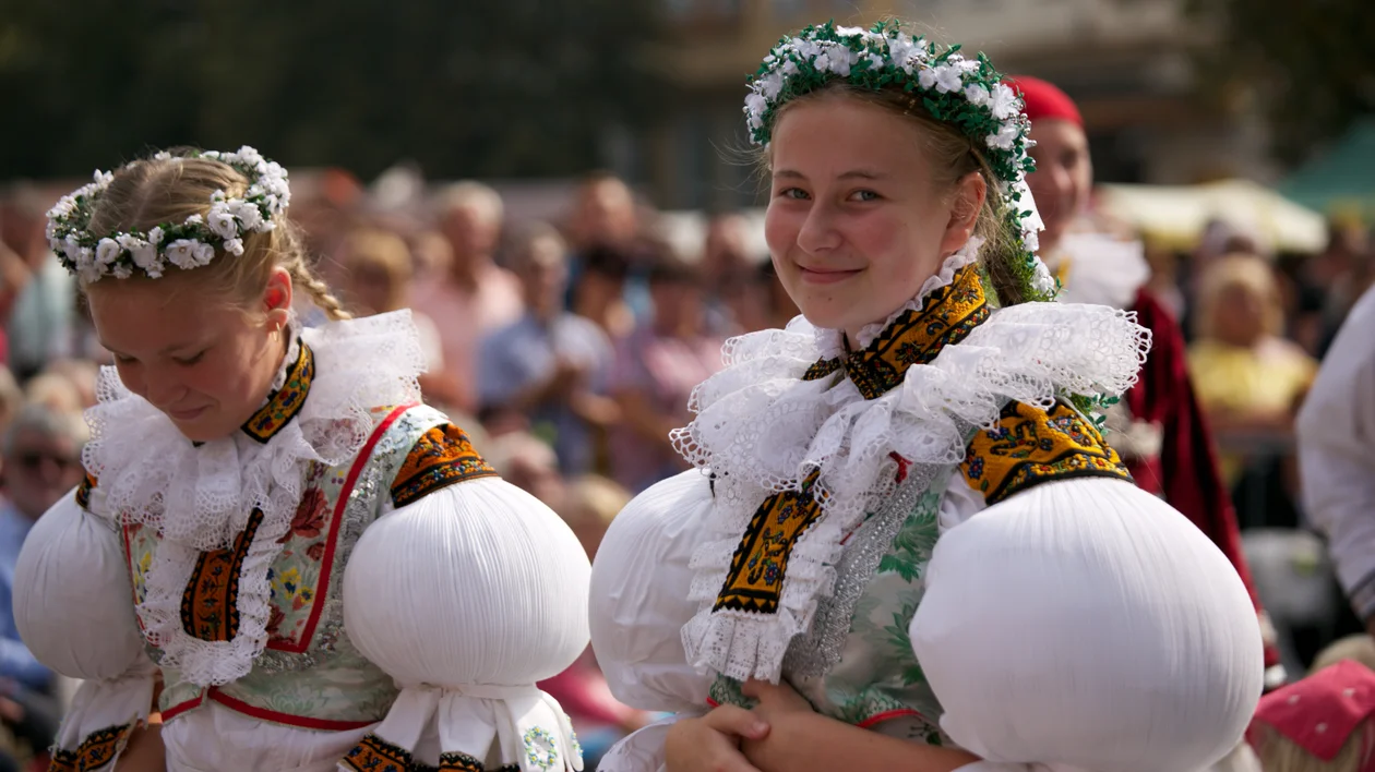 Girls in traditional European folk costumes with flower crowns at an outdoor festival.