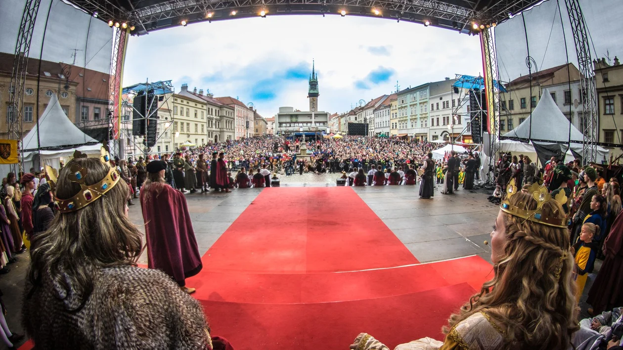 People in medieval costumes on stage facing a large crowd in a city square.