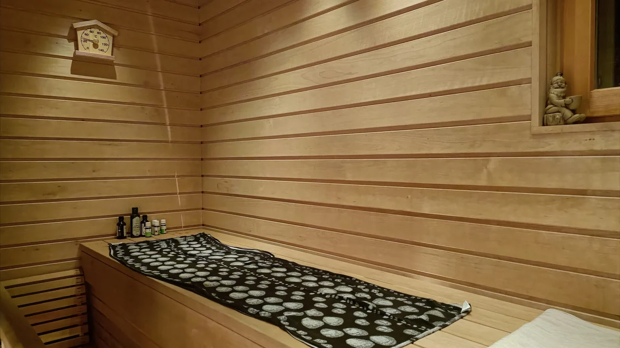Wood-paneled sauna room with a bench, patterned towel, and bottles on the side.