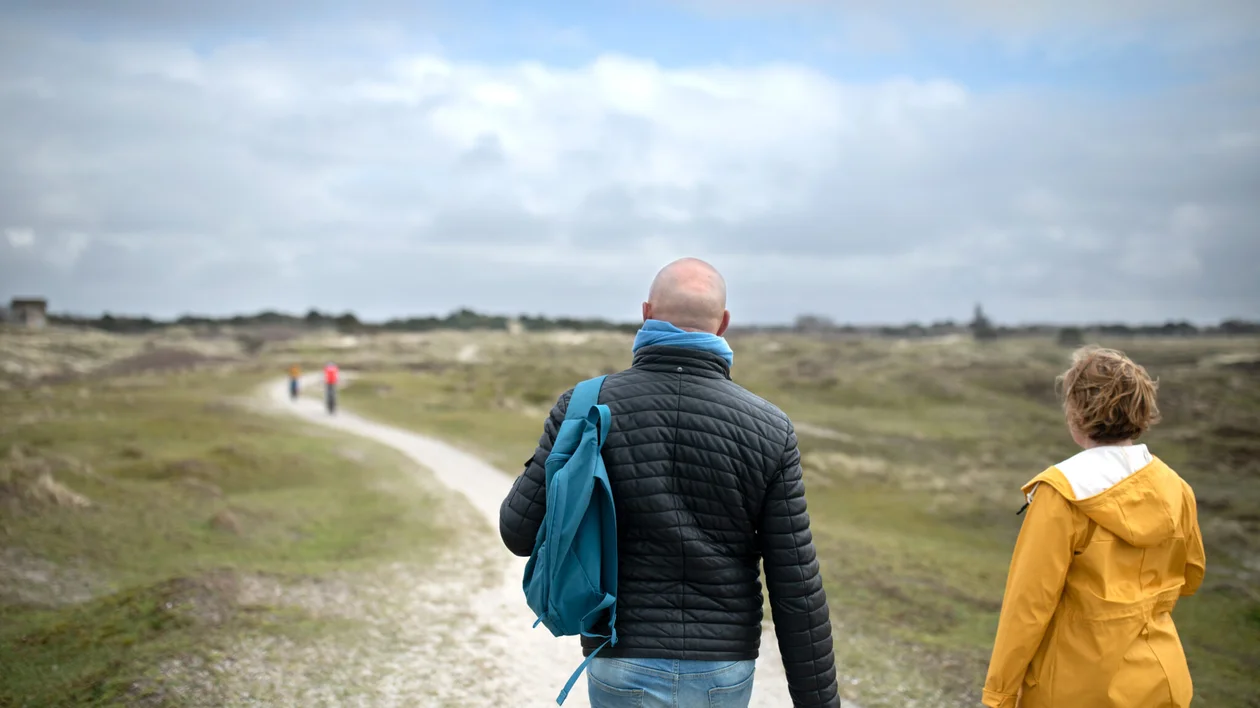Two people walking on a gravel path through a cloudy, grassy landscape.