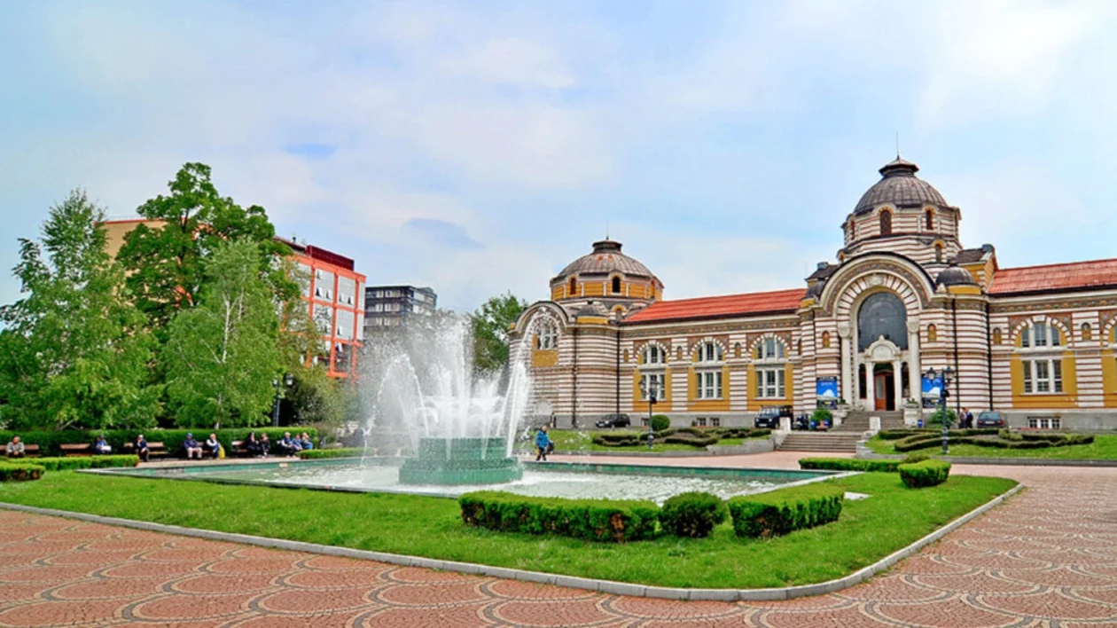 Fountain and manicured garden in front of a historic building with a domed roof.