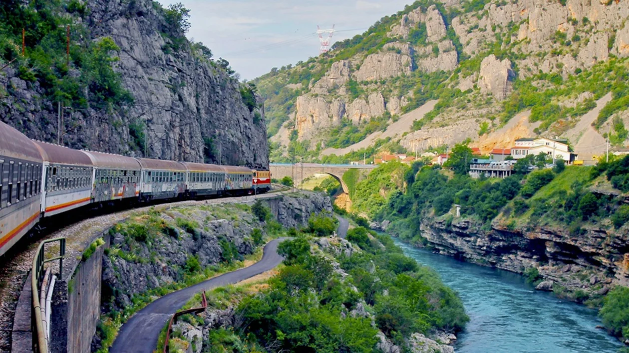 Train winding through a rocky mountain valley beside a turquoise river.