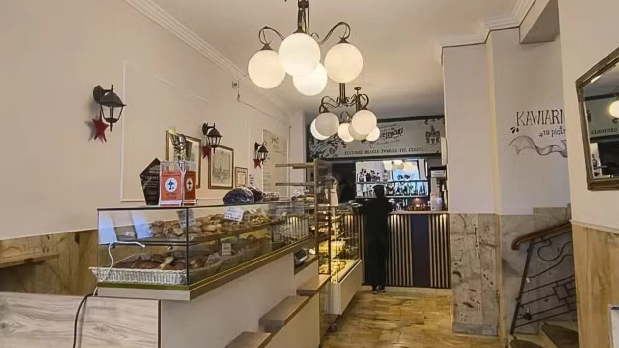 Bakery interior with pastry display case, warm lighting, and a person at the counter.