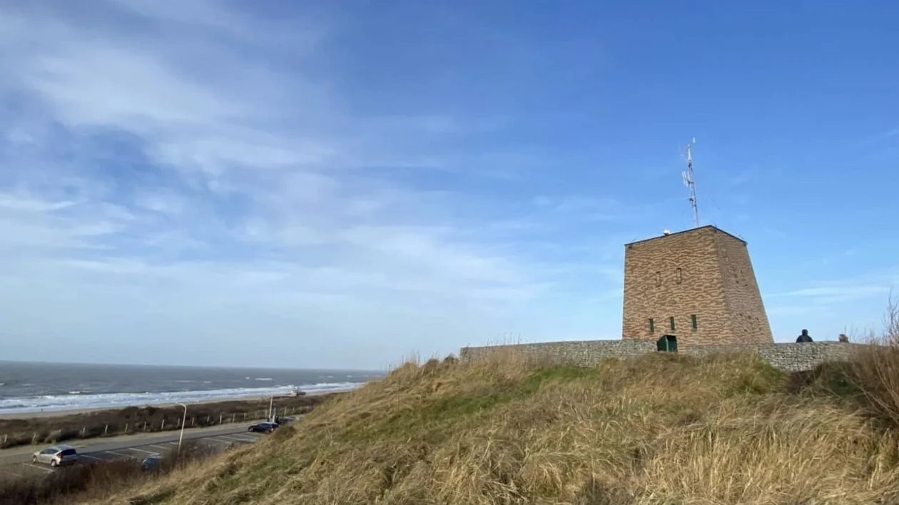 Stone tower on a grassy hilltop by the sea under a blue sky.
