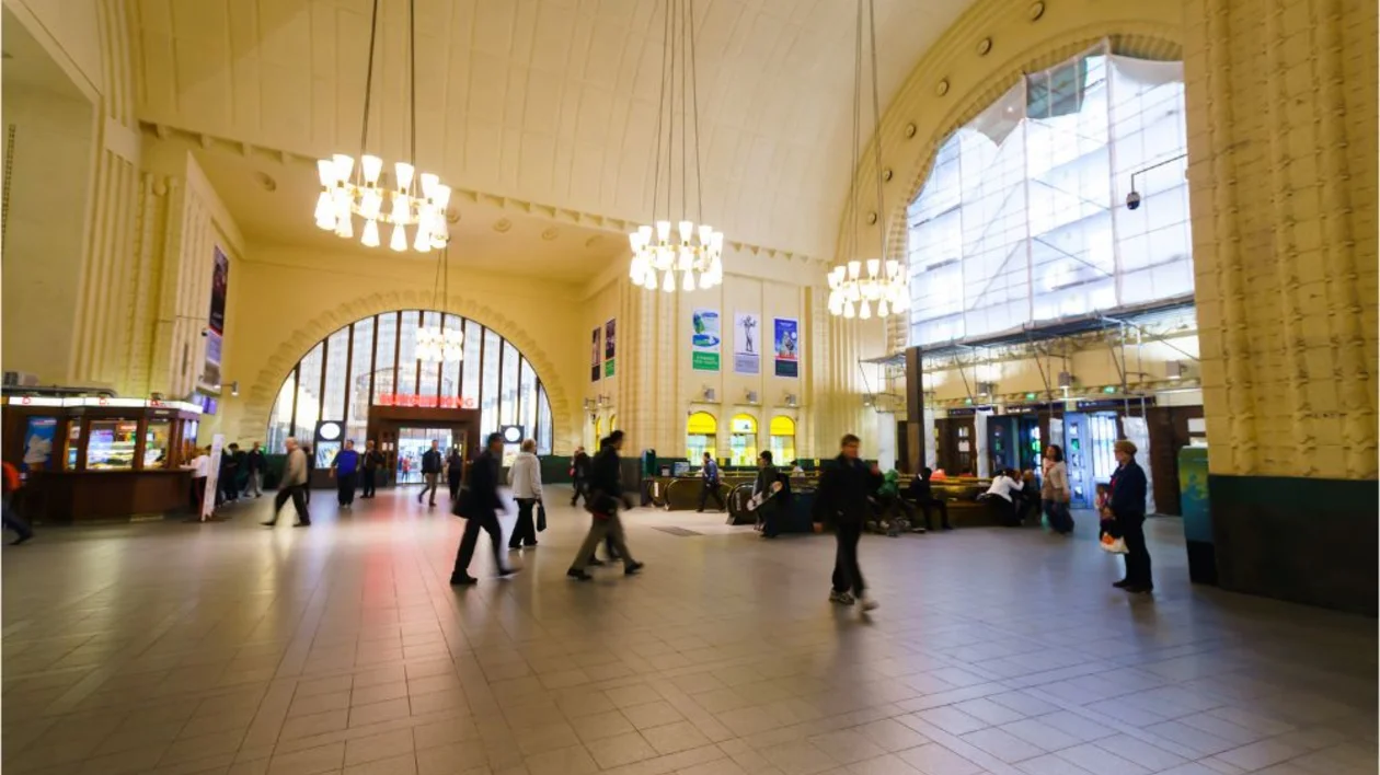 Spacious train station hall with high arched ceiling, large windows, and people walking.