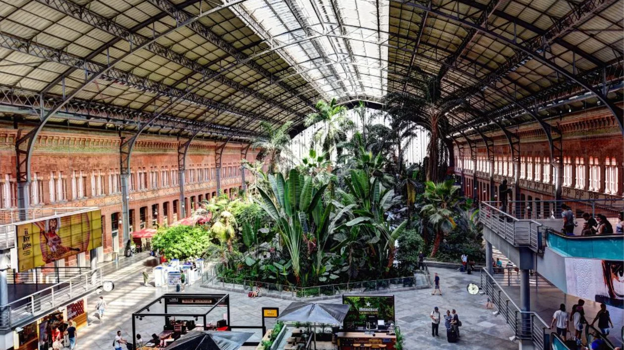 Indoor train station with a large tropical garden in the center and people walking around.