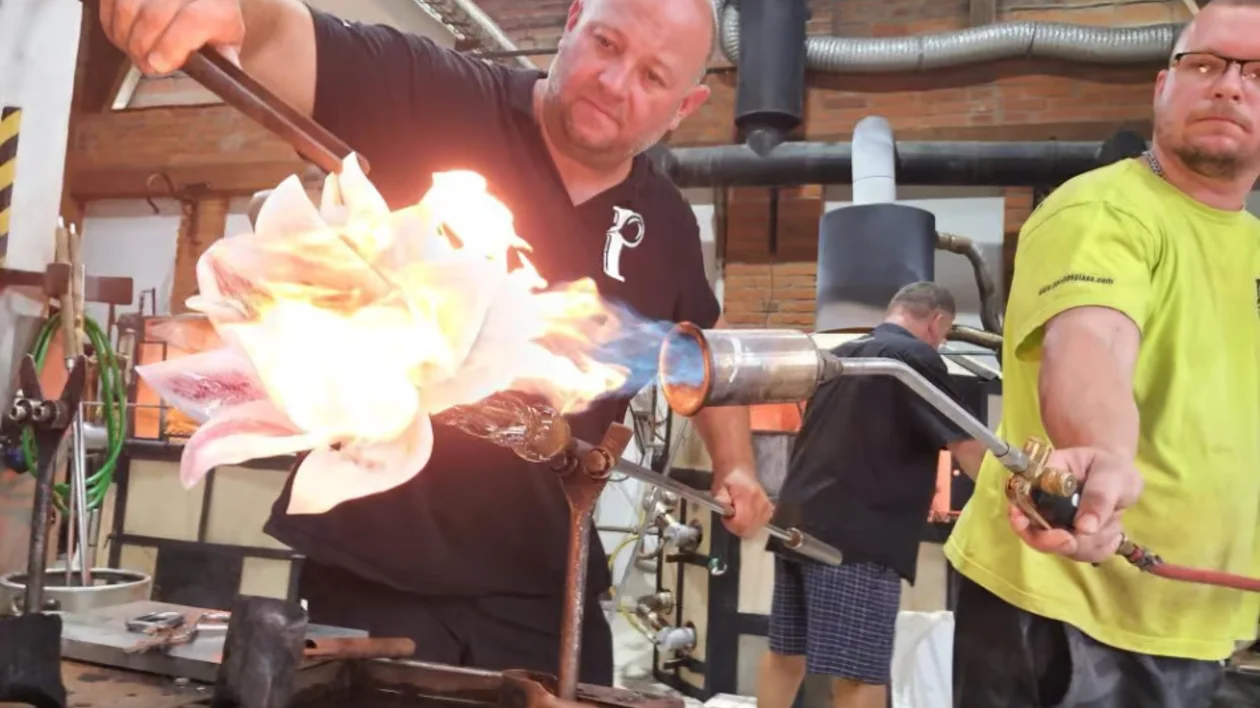 Two men shaping molten glass with tools in a workshop.