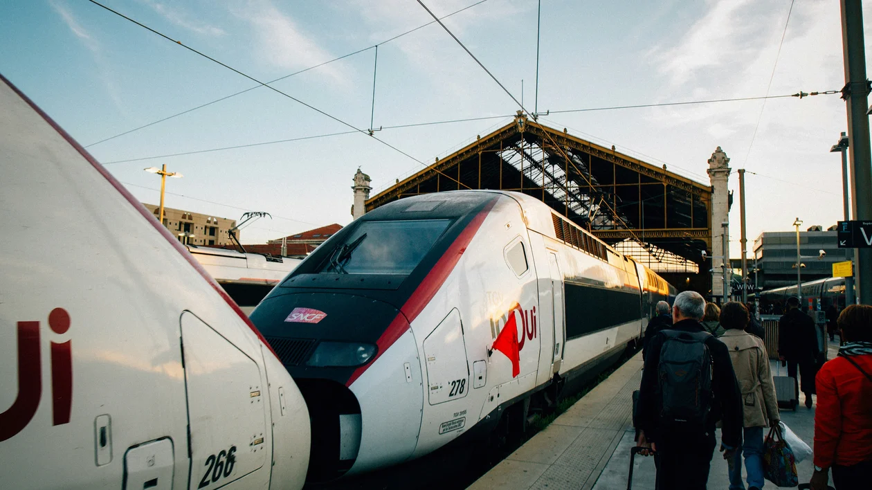 High-speed trains at a station platform with people walking alongside.