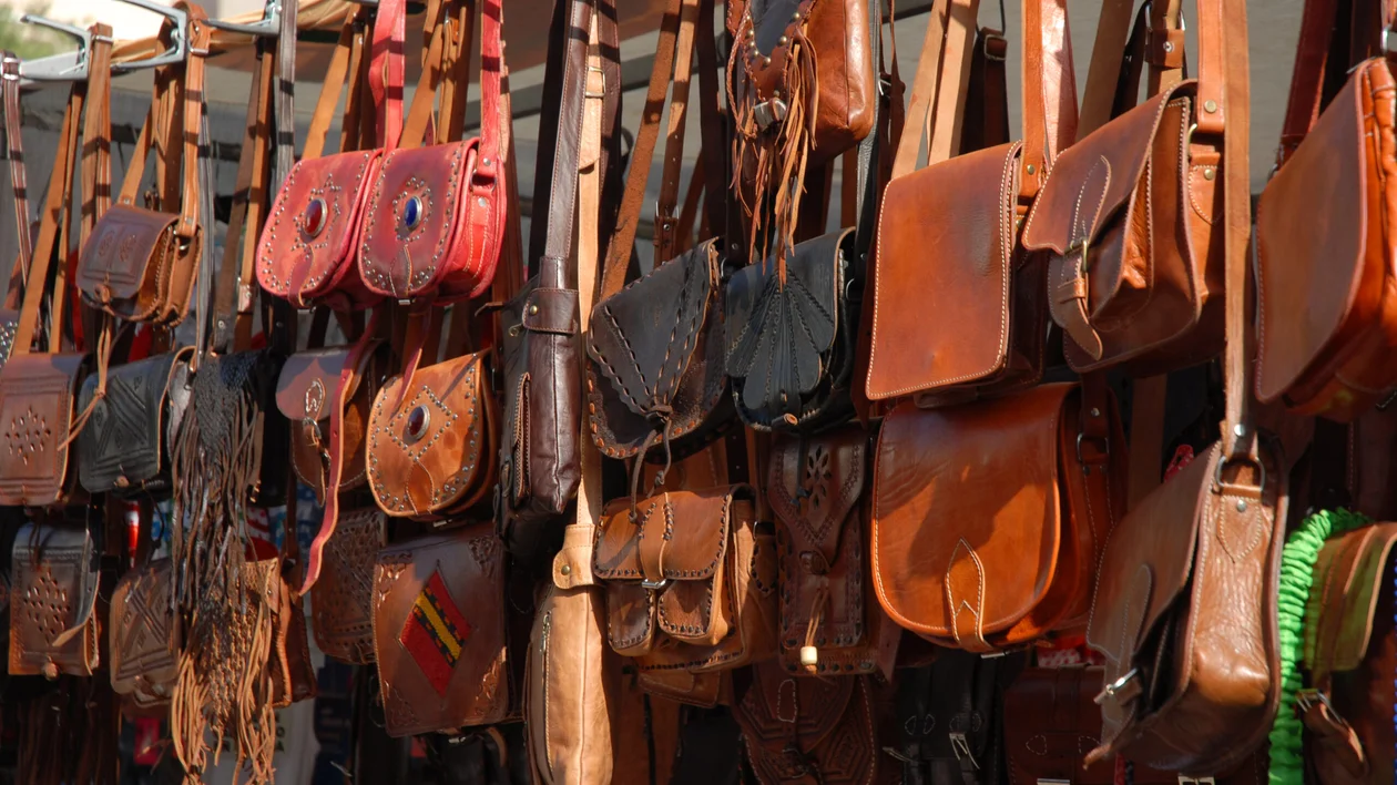 Rows of brown leather handbags hanging on display at an outdoor market.
