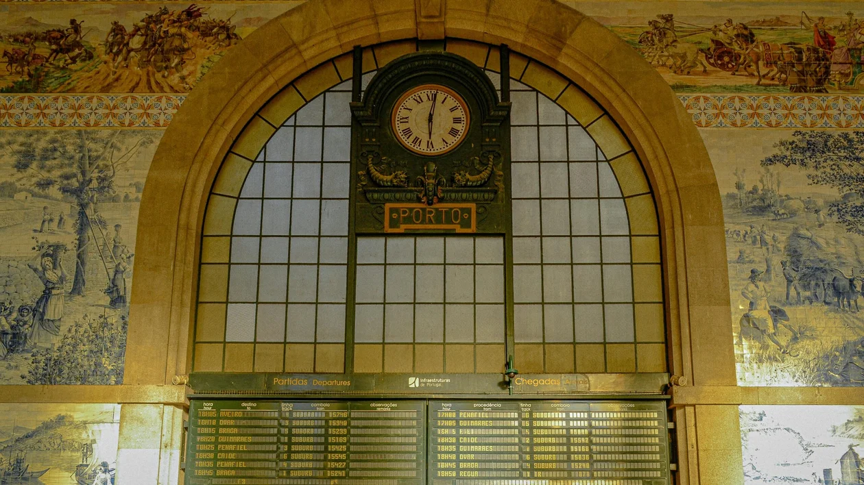 Large arched train station window with a clock and tiled mural decorations.