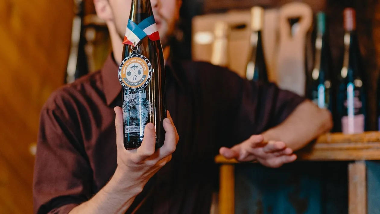 Person holding a wine bottle with a medal in a wine shop.