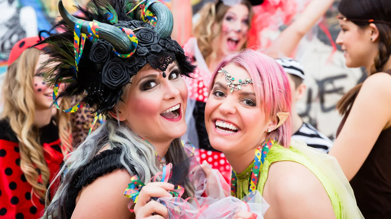 Two women in colorful, festive costumes smiling at a parade or party.