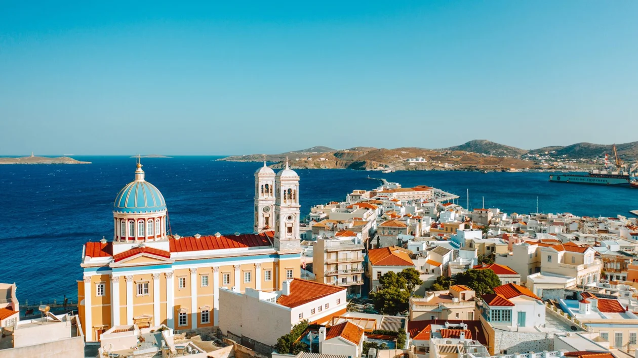 Coastal town with colorful rooftops, a domed church, and blue sea under a clear sky.