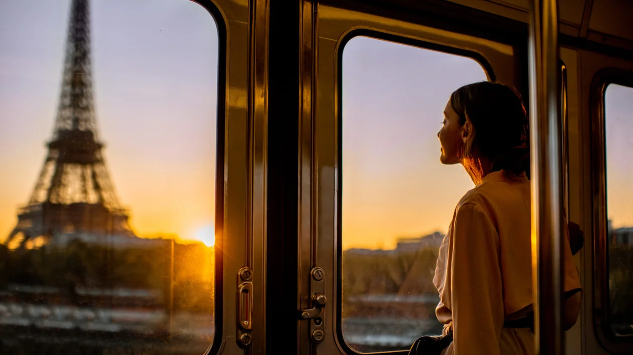 Woman on a train gazing at the Eiffel Tower during sunset.