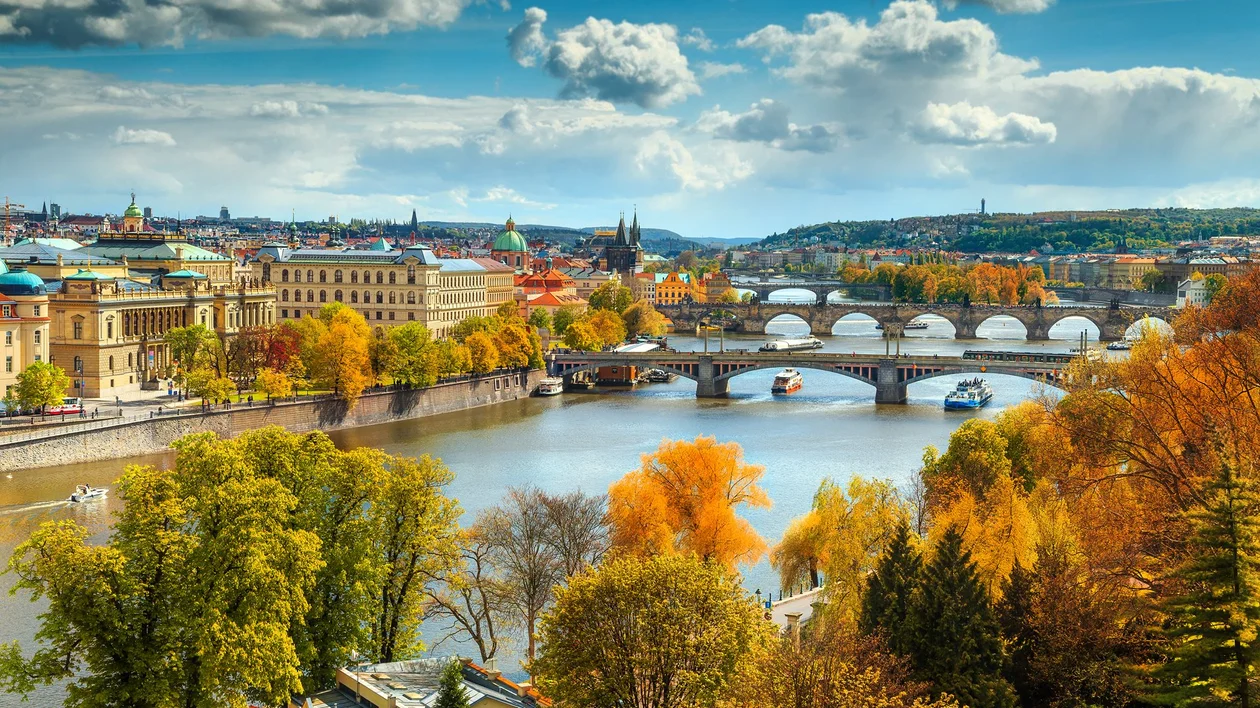 River with several bridges, colorful autumn trees, and historic city buildings under a cloudy sky.