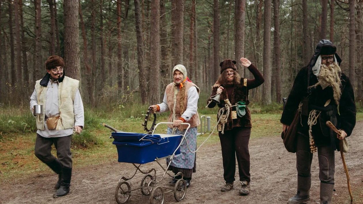 Four adults in costumes walk on a forest path, one pushing a stroller.