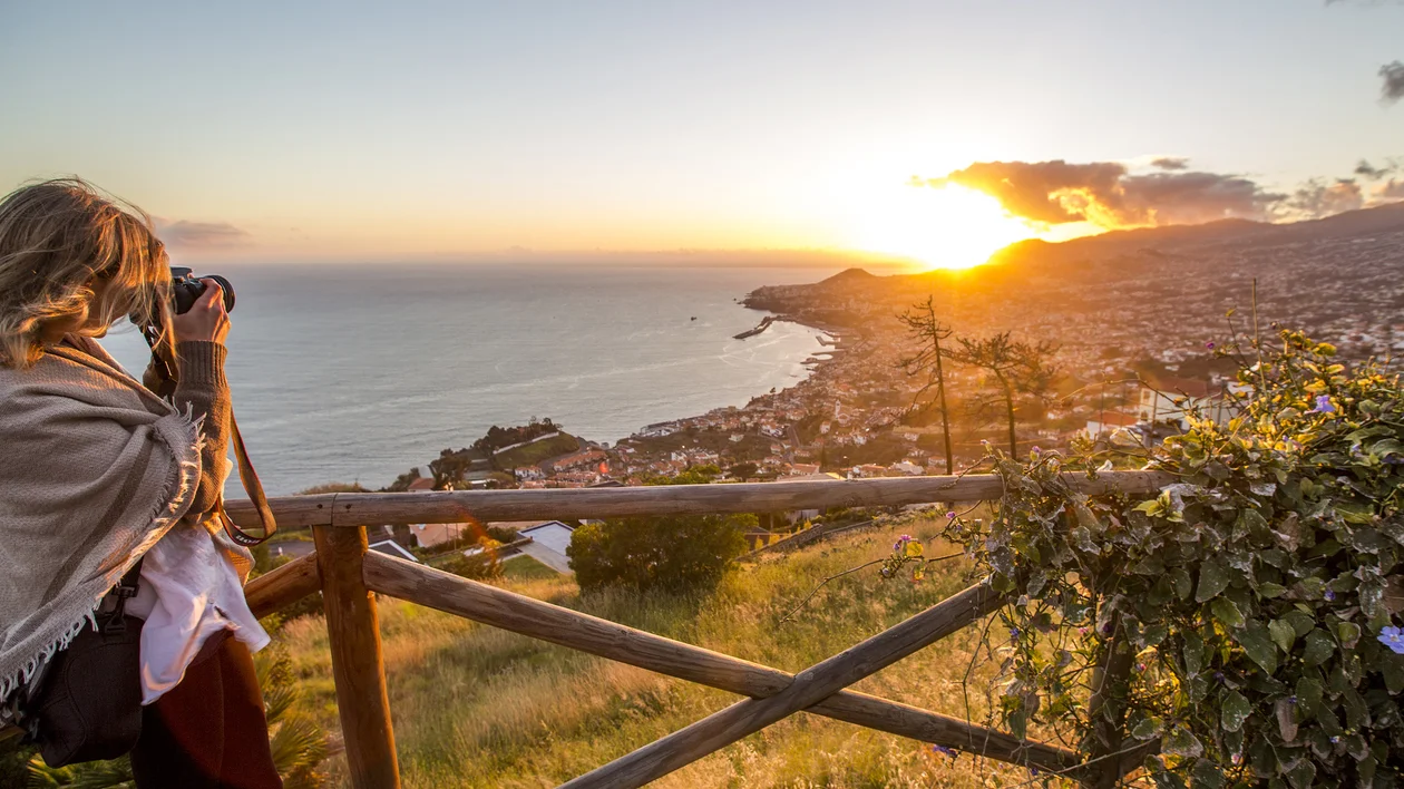 Woman photographing the sunset over Funchal and the Atlantic coast from Palheiro Village, Madeira, in autumn