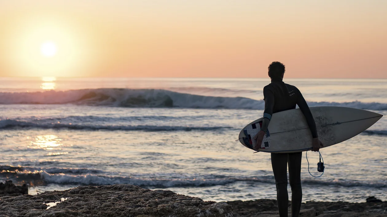 Surfer carrying a board and watching the waves at sunset in Ericeira, Portugal