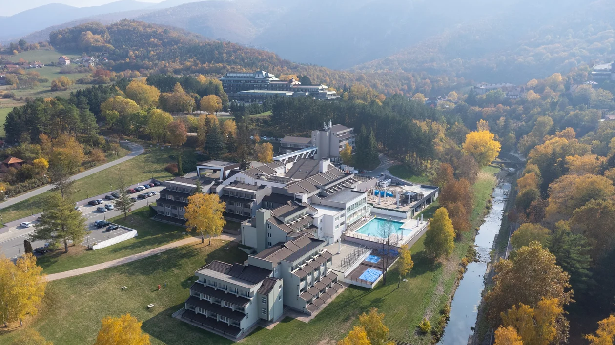 Aerial view of a modern hotel complex surrounded by autumn trees and mountains.