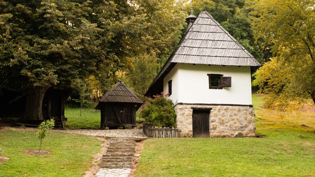 Small white cottage with a stone foundation surrounded by trees and grass.