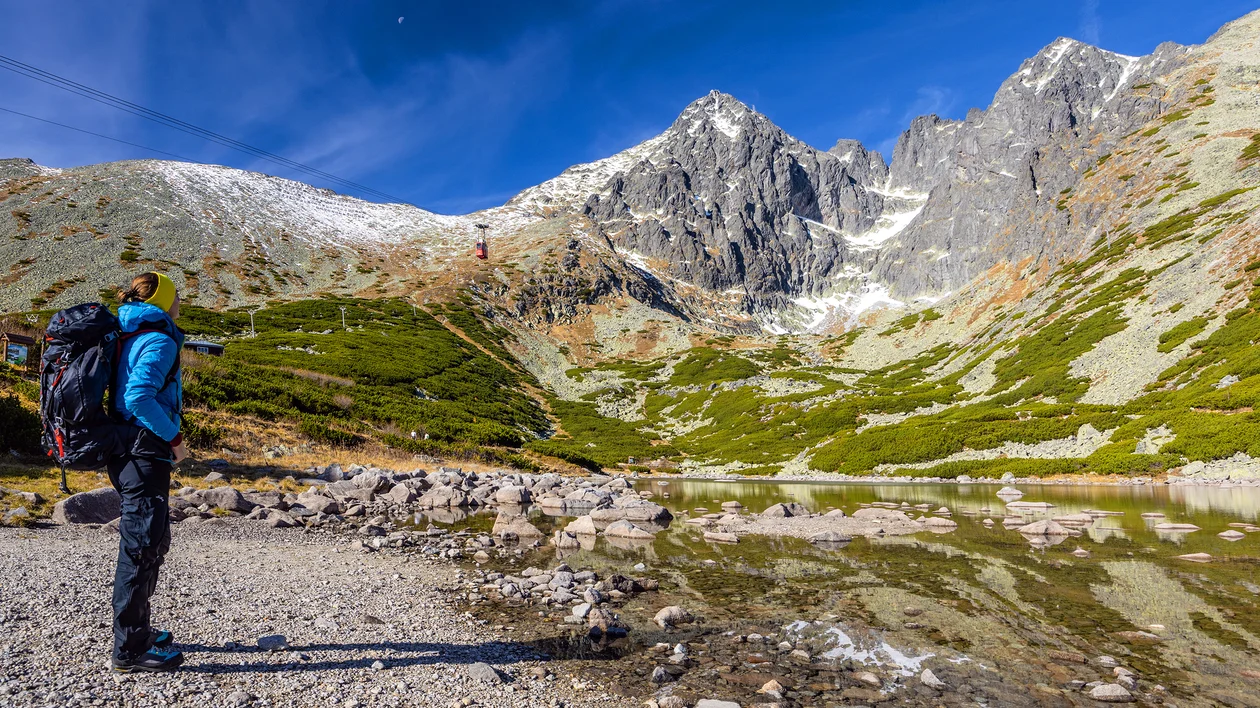 Hiker with backpack stands by a mountain lake under a clear blue sky.