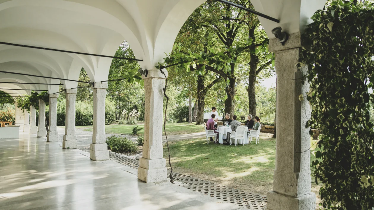 People sitting at a table in a garden, viewed from an arched walkway.