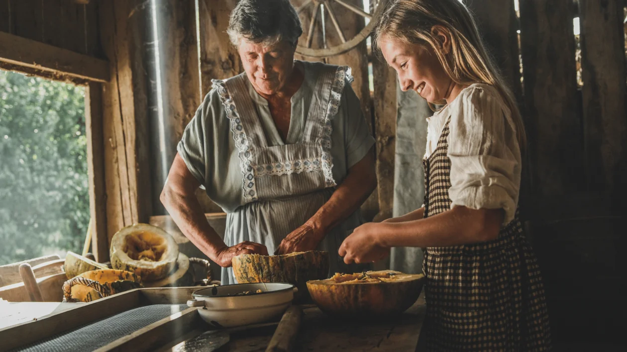 Older woman and young girl preparing squash together in a rustic wooden kitchen.