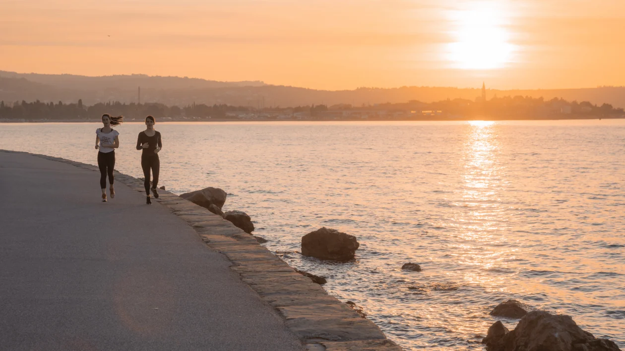 Two people jogging along a seaside path at sunset.