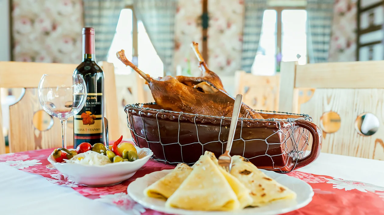 Roast duck, wine, crepes, and salad on a set dining table in a bright, cozy room.
