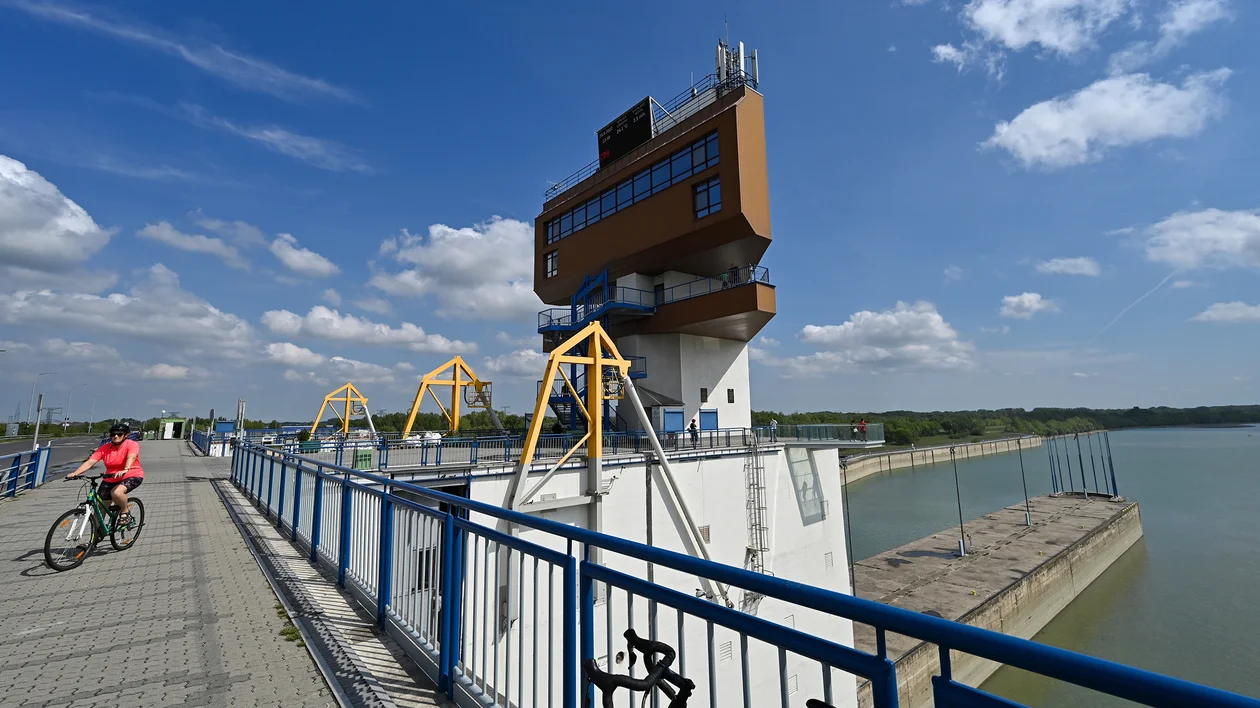 Cyclist on a river bridge near a modern building under a blue sky with clouds.