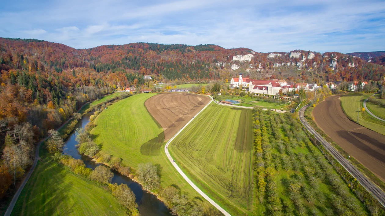 Aerial view of farmland, river, and a building with autumn trees in the background.