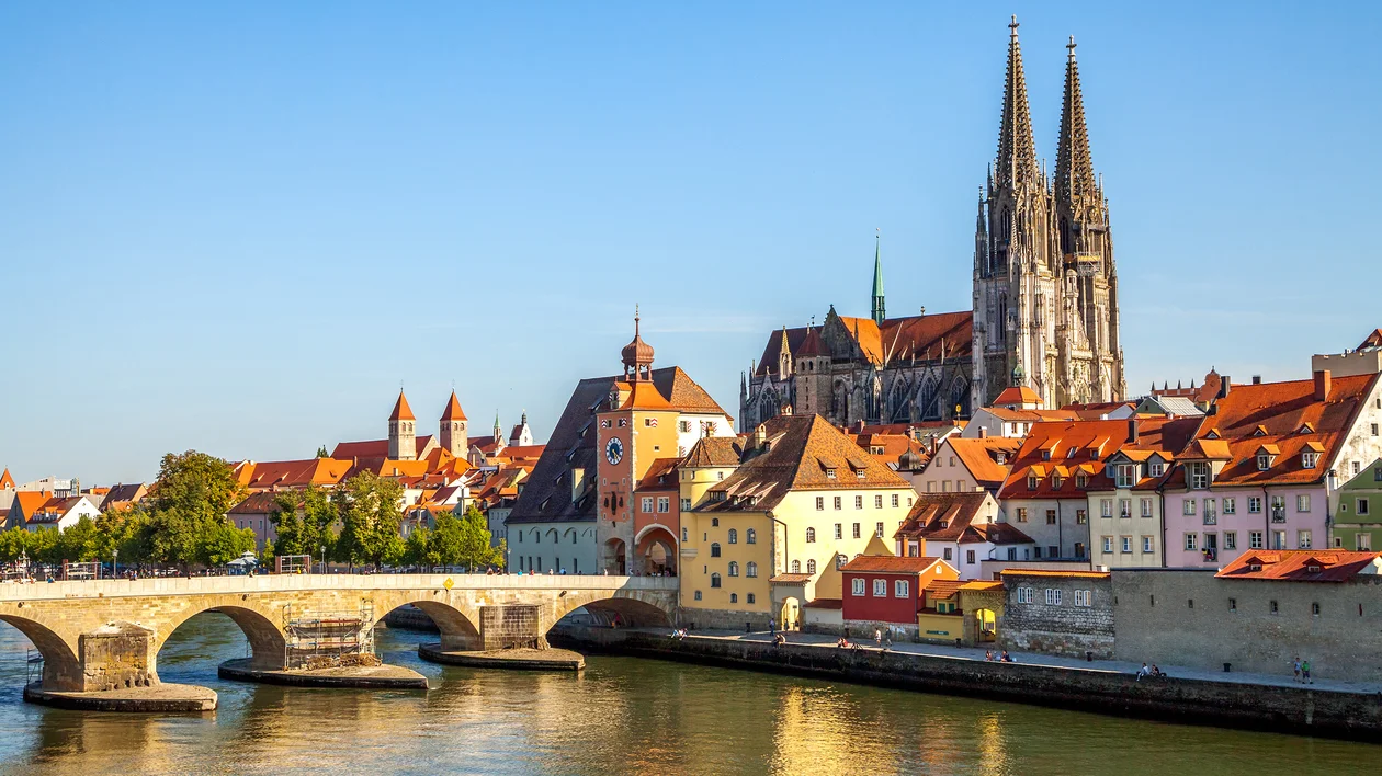 Colorful old town buildings and a cathedral beside a stone bridge over a river.