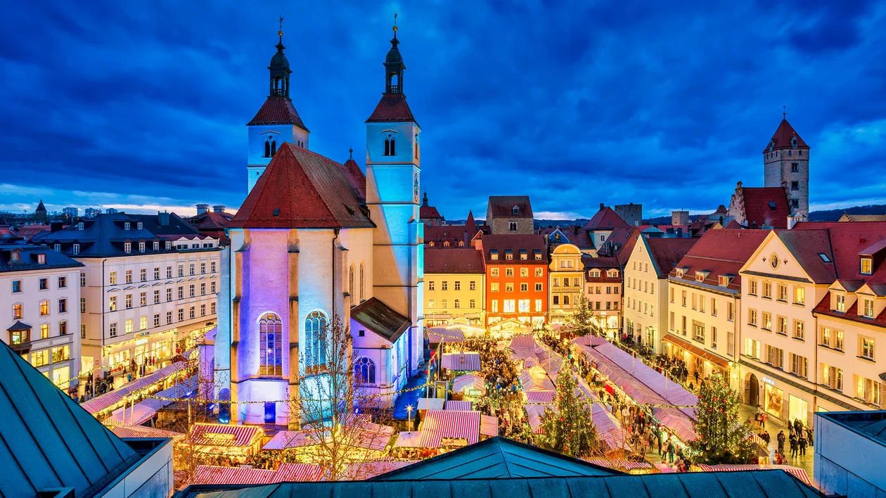 Town square with illuminated church, colorful buildings, and dramatic evening sky.