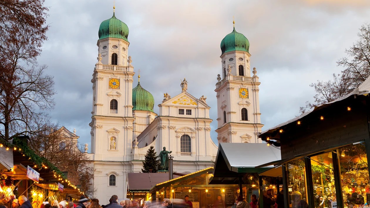 Christmas market stalls in front of a cathedral with green domes at sunset.