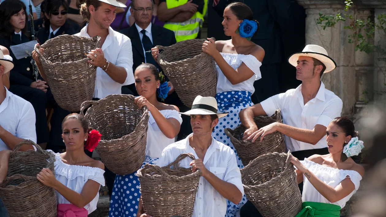 Group of dancers in traditional clothing holding large woven baskets outdoors.